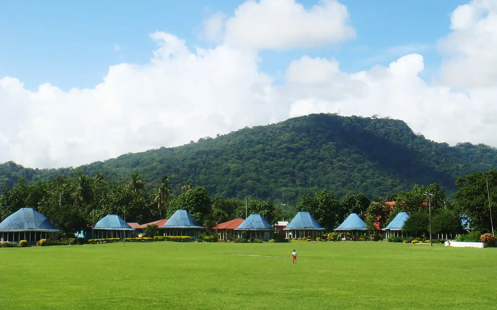 Round Samoan houses with blue roofs, Lepea village with Mt Vaea beyond